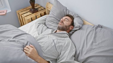 Orta yaşlı sakallı bir adam huzurlu bir şekilde modern bir yatak odasında uyuyor, rahatlık ve rahatlık simgeliyor..