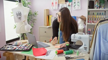 Dikiş malzemeleri ve ekipmanlarla çevrili renkli bir atölyede çalışan gözlüklü İspanyol kadın terzi..