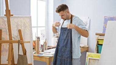 Parlak sanat stüdyosunda resim ve malzemelerle önlük ayarlayan yakışıklı bir adam.