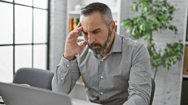 Ofis odasında sakallı ve gri saçlı düşünceli, olgun bir İspanyol adam. Konsantrasyonunu ve ciddiyetini ifade ediyor..
