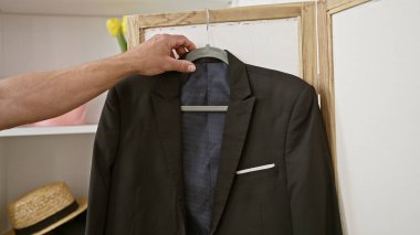 Giysi odasında takım elbise seçen bir adam olgun moda seçimlerini sembolize ediyor ve resmi bir etkinliğe hazırlanıyor..