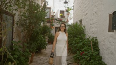 Genç İspanyol bir kadın locorotondo, puglia, İtalya 'nın büyüleyici beyaz sokaklarında yürüyor, yemyeşil ve tarihi mimariyle çevrili..