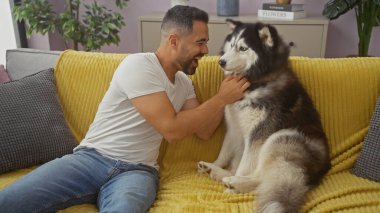 Neşeli, genç, İspanyol bir adam, dost canlısı kabuğuyla kapalı bir kanepede sevgi dolu bir şekilde etkileşime girer..