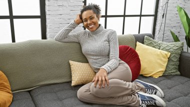 Oturma odasındaki renkli yastıklarla kanepede oturan gülümseyen kadın..