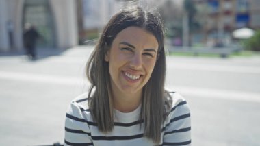 Güneşli bir şehir sokağında gülümseyen esmer saçlı, güzel, genç İspanyol bir kadın..