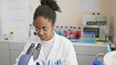 Afrikalı bir kadın bilim adamı laboratuvar ortamında mikroskop kullanarak örnekler inceleyerek sağlık hizmetleri araştırması yapıyor..