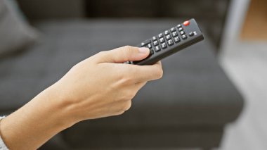 Modern bir oturma odasındaki koltukta otururken uzaktan kumandayı tutan biri..