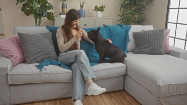 Genç İspanyol kadın ve Fransız bulldog köpeği rahat bir kanepede rahatlarlar..