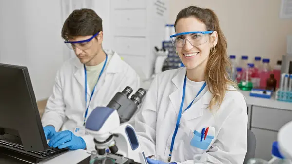 Stock image Man and woman in lab coats work as a team in a science laboratory, with microscope and computer.