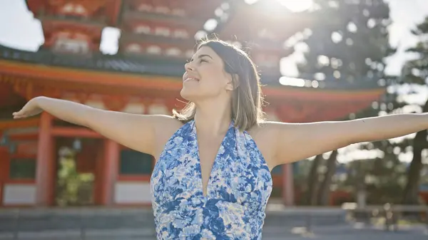 stock image Joyful hispanic woman, with beautiful open arms, confidently standing around heian jingu, kyoto, looking, smiling with freedom. radiating happiness, she enjoys the japanese temple's beauty.