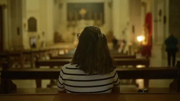 stock image A young hispanic woman sits alone in a beautiful historic christian church in italy, gazing towards the altar in quiet reflection.