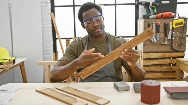 stock image A focused young man inspects timber in a woodwork studio, surrounded by tools reflecting his craft.