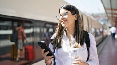 Tren istasyonunda akıllı telefon kullanarak demiryolunda yürüyen genç ve güzel bir İspanyol kadın.