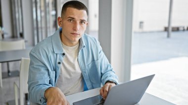 Genç bir İspanyol, üniversitenin kütüphanesinde laptopuyla çalışıyor. Kapalı alanda odaklanmış bir öğrenciyi canlandırıyor..