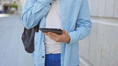 Kentsel caddede tablet kullanan, açık mavi ceketli, açık hava teknolojisi olan İspanyol bir adam..