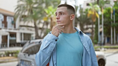 Düşünceli, genç, İspanyol bir adam şehir caddesinde dikiliyor, sıradan ve çekici bir tavır sergiliyor..