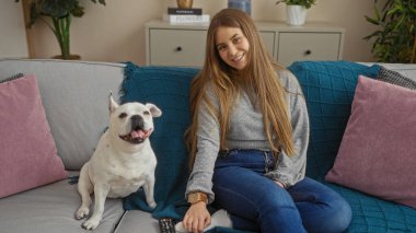 Genç sarışın bir kadın, kanepede rahat bir oturma odasında, yanında köpeğiyle oturuyor..