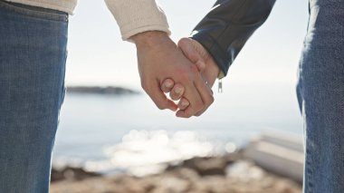 Deniz kenarında el ele tutuşan bir adam ve kadın, sakin bir okyanus zeminine karşı aşkı ve birlikteliği simgeliyor..