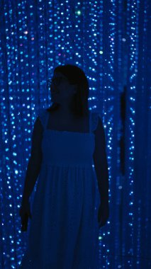 Işıl ışıl İspanyol kadın, gözlüklü güzel, modern müzedeki fütürist bir ışık sergisine daldırıyor, modern teknoloji ve yaratıcılığın floresan neon gösterimiyle yıkanıyor..