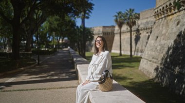 İspanya 'nın eski caddelerinde oturan genç İspanyol kadın tarihi şatonun yanında güneşli bir günün tadını çıkarıyor..