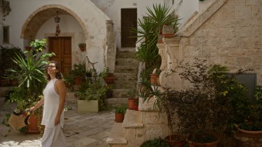 Genç bir İspanyol kadın, beyaz taş binalar ve Avrupa 'daki yemyeşil bitki yaşamının ortasında Locorotondo, Puglia' nın büyüleyici eski sokaklarında yürüyor..