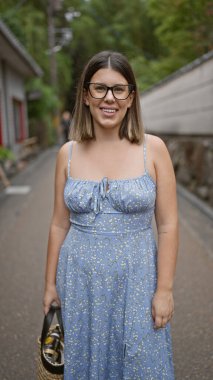 Kendine güvenen İspanyol kadın, güzel ve neşeli, gözlükleriyle neşeli poz veren, Kyoto 'nun geleneksel sokaklarında ayakta duran ve gülümseyen, doğal ve kaygısız Latin ifadesi yayan..