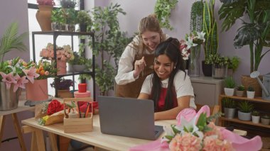 Çiçek ve çiçeklerle çevrili, çiçekçi dükkanında çalışırken gülümseyen iki kadın..