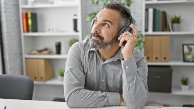 Ofiste gri sakallı, kulaklık takan düşünceli, olgun İspanyol bir adam..