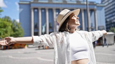 Güzel, genç İspanyol bir kadın, kendine güvenen, yaz şapkalı, kolları açık Nobel ödüllü bir binada duruyor.