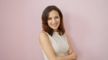 Kollarını kavuşturmuş gülümseyen genç bir İspanyol kadın pembe bir arka plana karşı duruyor, kendine güveni ve güzelliği yayıyor..