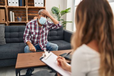 Stresli, sinirli ve hayal kırıklığına uğramış, tıbbi maskeli yaşlı bir adam bir psikoloji kliniğinde şok ve şaşkınlık içinde.