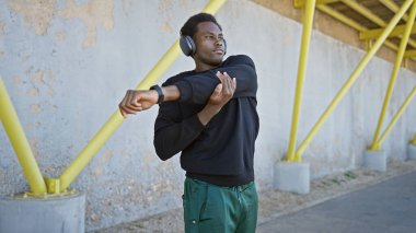 Afro-Amerikalı bir adam, şehir sokaklarında egzersiz yapmadan önce, kulaklık ve spor kıyafetleri takıyor..