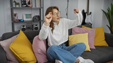 Kafkasyalı genç bir kadın, rahat bir oturma odasında neşeyle dans ediyor. Evdeki rahatlık ve rahatlığı somutlaştırıyor..