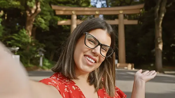 stock image Beautiful young hispanic woman, slipping on her glasses for a selfie at tokyo's meiji temple, showing the world her travel moments. smiling as she captures japanese culture on her smartphone