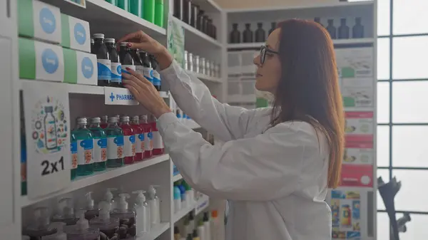 Stock image Redheaded woman pharmacist restocking medicines in a modern drugstore