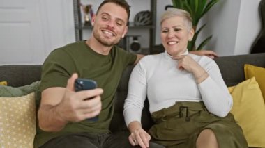 Kadın ve erkek oturma odasındaki bir kanepede birlikte oturuyor, akıllı bir telefonla meşgul, dalgınlıktan sevinçliliğe duygularını iletiyor..