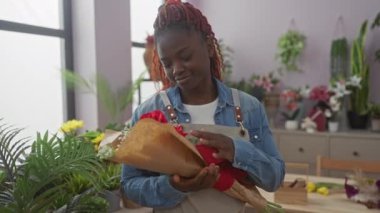 Gülümseyen genç Afrikalı bir kadın modern bir çiçekçide kırmızı güller düzenliyor. Girişimci ruhunu somutlaştırıyor.