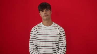 İspanyol asıllı genç adam çizgili tişört giyiyor. Mutlu bir şekilde duruyor. Yüzünde soğuk bir gülümseme var.