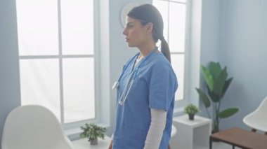 Kendine güvenen bir kadın hemşire kollarını kavuşturur. Parlak bir klinik odasında, pencereleri ve bitkileri olan..