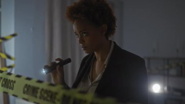 Afrika kökenli Amerikalı kadın dedektif, kapalı bir olay yerini, el fenerini ve dikkat bandını inceliyor..