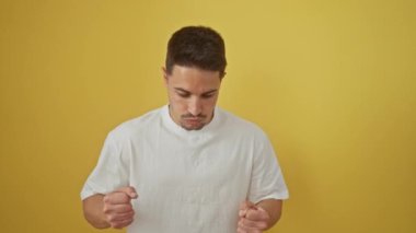 Beyaz tişörtlü hayal kırıklığına uğramış genç İspanyol adam çılgına dönüyor, bağırıyor, kolları sallanıyor, yüzü öfkeden çatlıyor! Öfkeli suratı, izole edilmiş sarı arka planda saf öfke diye haykırıyor..