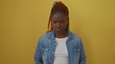 Sinirli Afro-Amerikalı kadın, üzgün ve kuşkucu, kot gömlek içinde, yüzünde derin bir kökü olan somurtkan gösteren, canlı sarı bir arka plan karşı izole