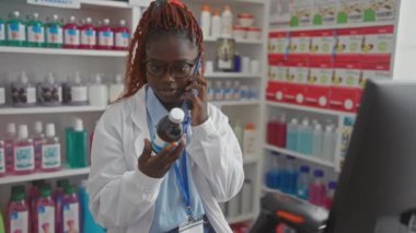 Eczanede telefonla ilaç şişesini inceleyen genç bir kadın eczacı..