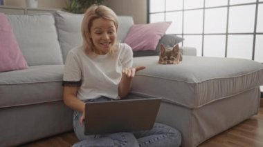 Sarışın, beyaz, genç bir kadın oturma odasında Chihuahua köpeği yanındayken video görüşmesi yapıyor. Ev ortamında rahat bir ortam sergiliyor..