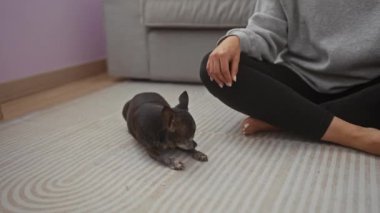 Gündelik giysiler içindeki bir kadın evde küçük köpeğiyle birlikte desenli bir zeminde uzanıyor..