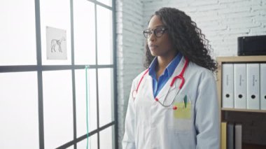 Beyaz tuğla duvarlı ve arka planda penceresi olan bir veteriner kliniğinde kolları çapraz duran kıvırcık saçlı Afrikalı Amerikalı kadın veteriner..