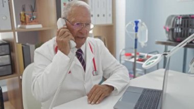 Bir veteriner kliniğinde dizüstü bilgisayar ve tıbbi malzemelerle kıdemli erkek doktor telefonda..