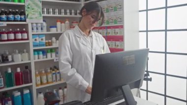 Kendine güvenen bir kadın eczacı modern, iyi stoklanmış bir eczanede bilgisayarın başında çalışıyor..