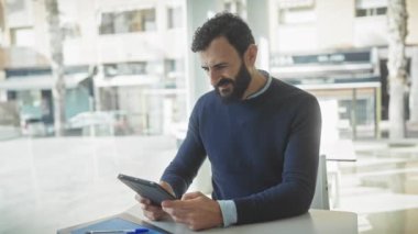 Kendine güvenen işadamı, modern ofis ortamında tablet kullanıyor, günlük giysiler giyiyor, sakallı, kapalı mekanlı..