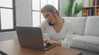 Modern bir oturma odasında akıllı telefon ve dizüstü bilgisayarla birden fazla iş yapan genç bir kadın.